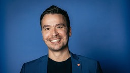 Porträtaufnahme des Influencers und Lehrers Bob Blume im blauen Sakko vor blauem Hintergrund.