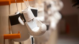 Weiße Boxhandschuhe hängen an einer Garderobe in einem Trainingsraun