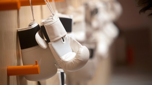 Weiße Boxhandschuhe hängen an einer Garderobe in einem Trainingsraun