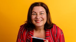 Eine Porträtaufnahme von Christina Bacher vor orangenem Hintergrund.