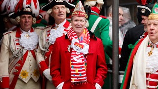 Christoph Kuckelkorn, Präsident des Festkomitees Kölner Karneval und Organisator des Kölner Rosenmontagzugs in Karnevalskostüm mit Narrenkappe und Karnevalsschal inmitten karnevalistisch verkleideter Funken an Weiberfastnacht 2026 in Köln