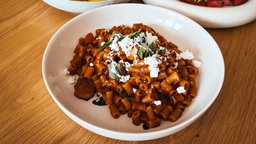Das griechische Gericht "Chtapodi me kofto marakonaki" wurde auf einem weißen Teller serviert – als Zutaten sind Makkaroni, Oktopus, Tomate, Salbei und Feta zu erkennen.
