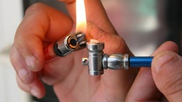 Nahaufnahme auf Hände die mit einem Feuerzeug eine Crack-Pfeife anzünden.