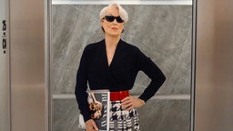 Meryl Streep steht in der Rolle der RUNWAY-Chefredakteurin Miranda Priestly in "Der Teufel trägt Prada 2" mit Magazin und Sonnenbrille in einem Aufzug