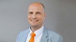 Ein Porträt von  Prof. Dominik Enste in Anzug und Krawatte vor grauem Hintergrund.