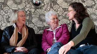 Drei Frauen sitzen auf einem Sofa und unterhalten sich. 
