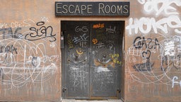 n einer mit Graffiti beschmierten Wand befindet sich eine schwere Tür, über der „Escape Rooms“ steht.