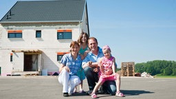Familie posiert für ein Foto vor ihrem neuen Eigenheim. 