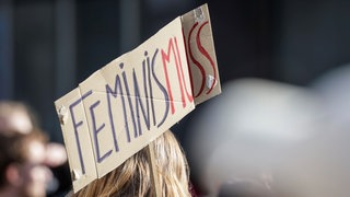 Ein Teilnehmerin einer Demonstration zum Weltfrauentag trägt ein Schild mit der Aufschrift "Feminis-muss".