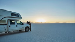 Zwei Menschen mit einem Camper am Salzsee Salar de Uyuni, Bolivien