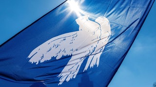 Fahne mit einer Friedenstaube vor blauem Himmel. 