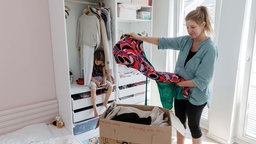 Frau packt Kleidung in einen Karton. 