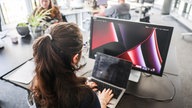 In einem Großraumbüro eines Startup-Hubs "Startplatz" arbeitet eine Frau an Laptop und Monitor