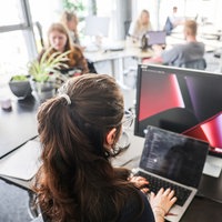 In einem Großraumbüro eines Startup-Hubs "Startplatz" arbeitet eine Frau an Laptop und Monitor