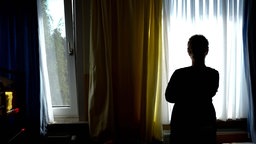 Eine junge Frau in einem dunklen Zimmer vorm Fenster. 