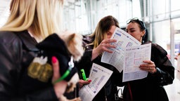 Eine Besucherin trägt einen Hund auf dem Arm, während andere im Hintergrund im Ausstellungsplan blättern, bei der Jobmesse für Geflüchtete "FuTog Berlin".