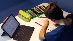 Ein Schüler erledigt seine Hausaufgaben mit Heft, Stift und Laptop
