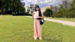 Eine junge Frau steht auf einer Wiese und hält ihre Wahlbenachrichtigung zur Integrationsratswahl in der Hand.