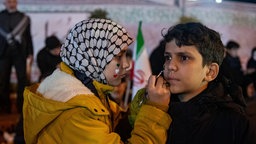 Ein Mädchen in Teheran malt Herzen auf das Gesicht eines Jungen.
