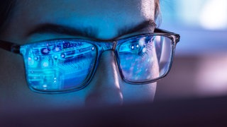 Mann mit Brille, in der sich Computertechnik spiegelt