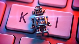 Ein kleine Roboterfigur liegt auf einer Tastatur mit den Buchstaben "KI"