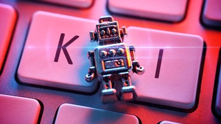 Ein kleine Roboterfigur liegt auf einer Tastatur mit den Buchstaben "KI"