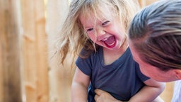 Ein kleines Mädchen lacht ausgelassen, während es von einer Frau ausgekitzelt wird