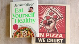 Die beiden Kochbücher "Eat yourself healthy" und "In pizza we crust" liegen auf einem Tisch. 