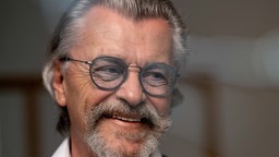 Nahaufnahme von Manfred Gotta mit grauem Haar, Brille mit bläulichen Gläsern und grauem Bart.
