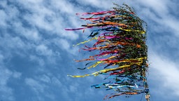 Maibaum mit bunten Bändern weht im Wind vor blauen Himmel