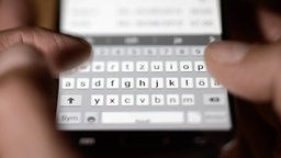 Nahaufnahme von Fingern, die über die digitale Tastatur eines Smartphones tippen.