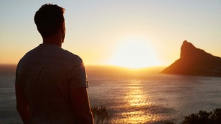 Junger Mann steht auf Klippe am Meer und genießt den Ausblick. 