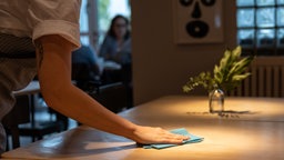 Symbolbild Minijob in der Gastronomie: Eine Person wischt einen Tisch in einem Café ab