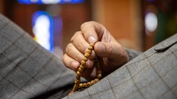 Detailaufnahme einer Hand die eine "Misbaha", eine islamische Gebetskette, hält.