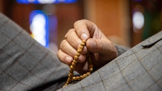 Detailaufnahme einer Hand die eine "Misbaha", eine islamische Gebetskette, hält.