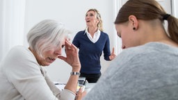 Drei Frauen sitzen in einem Büro und streiten sich. 