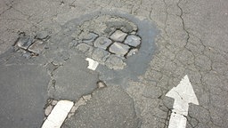 Pfeile und aufgebrochene Straßendecke auf einer maroden Straße in einem Wohnviertel