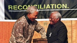 Der damalige südafrikanische Präsident Nelson Mandela (l) bekommt am 29.10.1998 in Pretoria fünf dicke Bücher vom Erzbischof Desmond Tutu überreicht. 