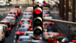 Nahaufnahme einer roten Ampel; verschwommen im Hintergrund ist eine Straße mit hohem Verkehrsaufkommen zu sehen.