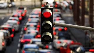 Nahaufnahme einer roten Ampel; verschwommen im Hintergrund ist eine Straße mit hohem Verkehrsaufkommen zu sehen.