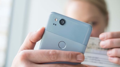 Eine Frau hält ein Smartphone und einen Personalausweis in den Händen, um am Video-Ident-Verfahren teilzunehmen. 