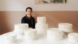 Konditorin und Inhaberin sitzt in ihrem Café und Cake Studio "Polz" in Köln-Ehrenfeld an einem Tisch voller heller, verzierter Torten