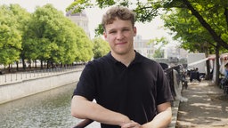 Porträtaufnahme von Quentin Gärtner: Ein junger Mann mit kurzem, hellem, lockigem Haar, leicht zusammengekniffenen blauen Augen und einem schwarzen T-Shirt.