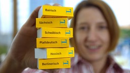 Eine Frau hält kleine Wörterbücher in verschiedenen Dialekten in der Hand.