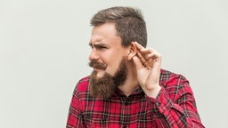 Ein Mann mit Vollbart hält sich die Hand ans Ohr, um zu zeigen, dass er schlecht hört.