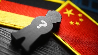 Symbolfoto chinesische Spionage: Schwarze Figur mit Fragezeichen auf den Flaggen von Deutschland und China. 