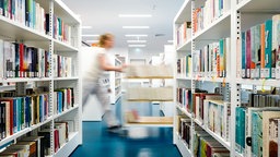 Eine Frau schiebt auf einem Wagen Bücher durch die Räume einer Bibliothek