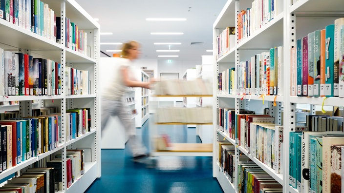 Eine Frau schiebt auf einem Wagen Bücher durch die Räume einer Bibliothek