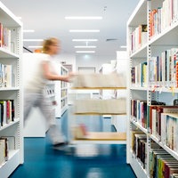 Eine Frau schiebt auf einem Wagen Bücher durch die Räume einer Bibliothek
