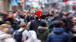 Mitten in einer hektischen Menschenmenge steht eine einzelne Person mit Weihnachtsmütze.